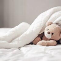 Cute little teddy bear lying sleeping alone on white bed in morning, generative ai